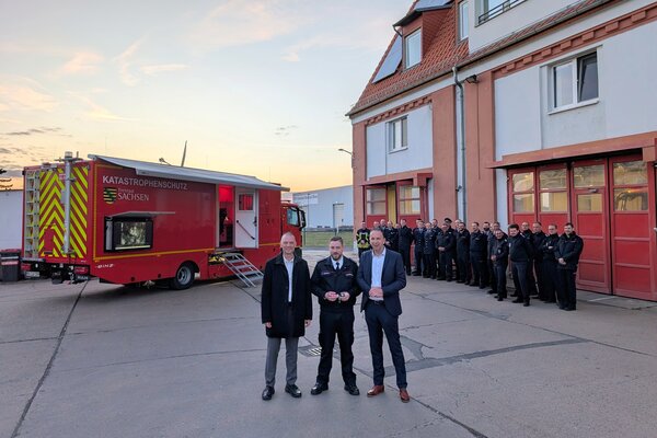 Landrat Ralf H&auml;nsel, Riesas Stadtwehrleiter Robert Gudat und Oberb&uuml;rgermeister Marco M&uuml;ller (v. l.) mit den Kameraden und dem neuen Einsatzleitwagen 2