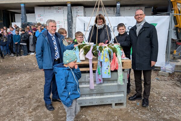 Gregor Drews, Ingrid Stier und Landrat Ralf H&auml;nsel (v. l.) mit Sch&uuml;lerinnen und Sch&uuml;lern am geschm&uuml;ckten Richtkranz