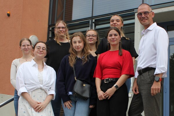 Gruppenbild sieben Auszubildender und Landrat Ralf H&auml;nsel vor der Eingangst&uuml;r des Landratsamtes.