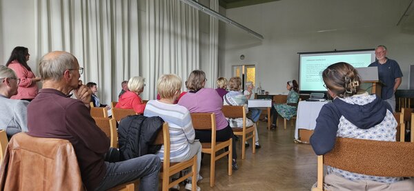 Bild vergr&ouml;&szlig;ern: Sitzende Menschen in einem Raum, die nach vorne zu den Vortragenden schauen.